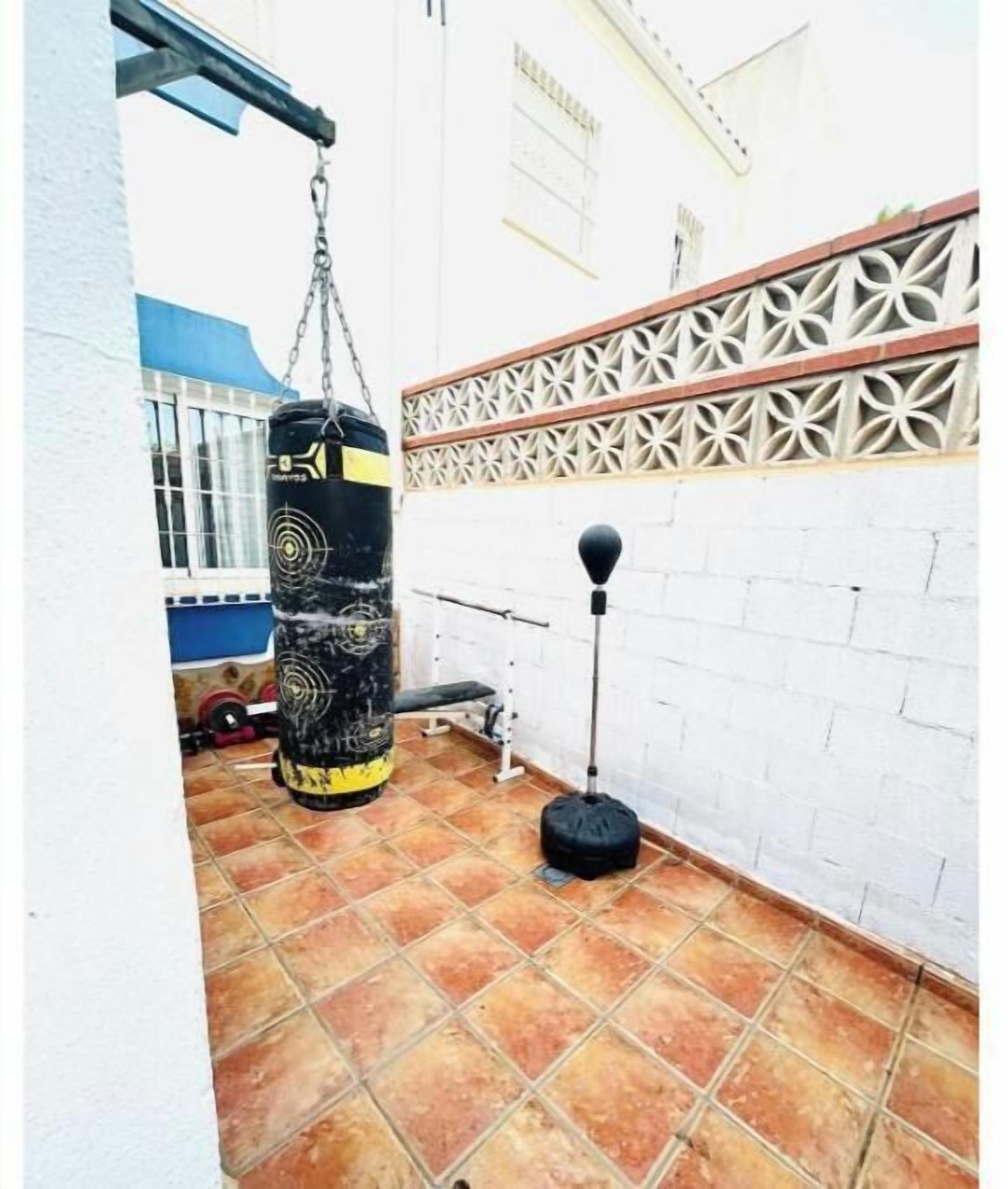 Un petit espace extérieur aménagé pour faire de l’exercice, avec un sac de frappe, une corde à sauter et un banc.