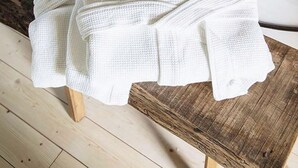 A bed with a metal headboard and a wooden bedside table with a white towel and white pants on it.
