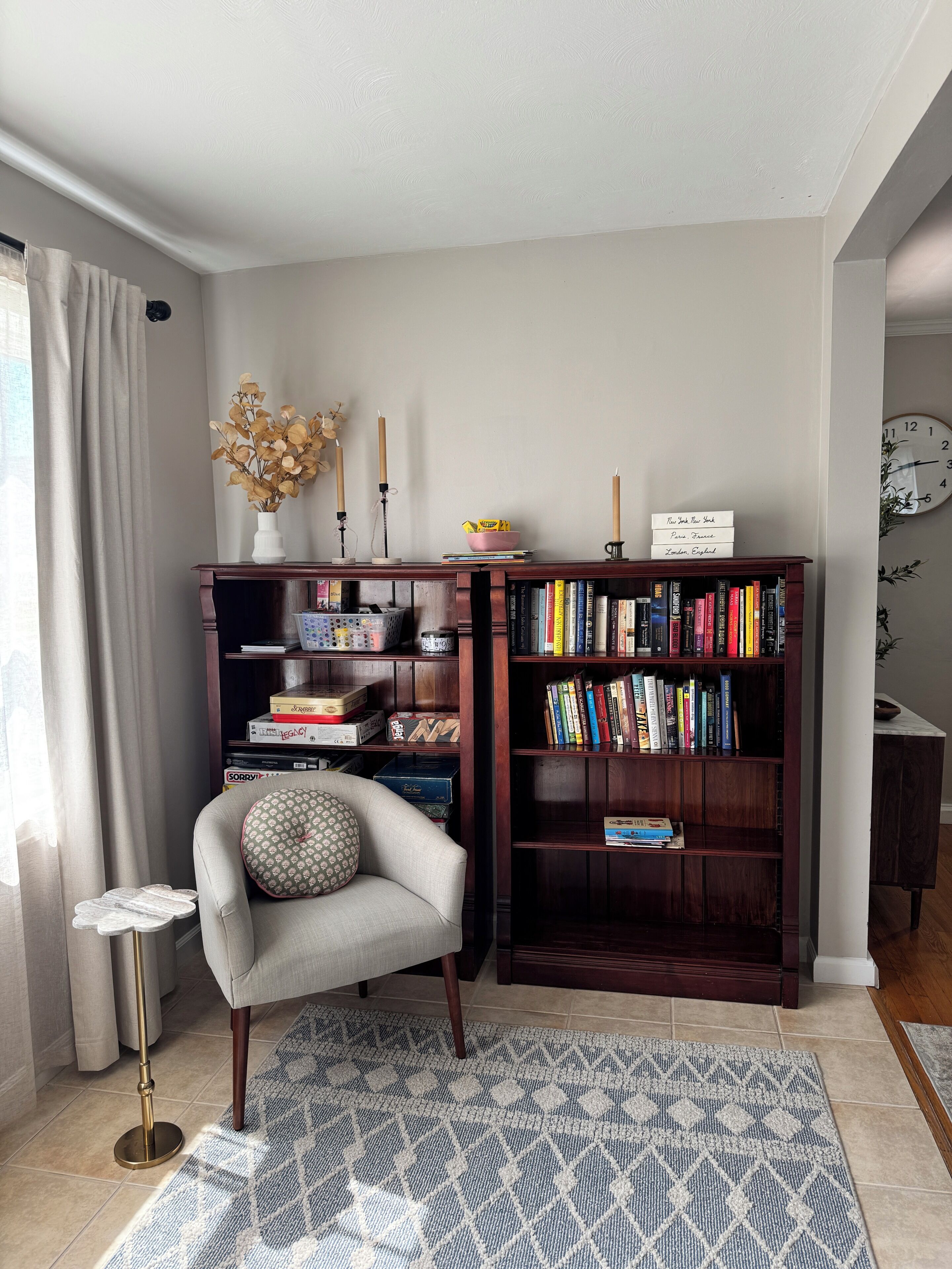Una habitación de esquina con una estantería, una silla, una mesita y un reloj en la pared.
