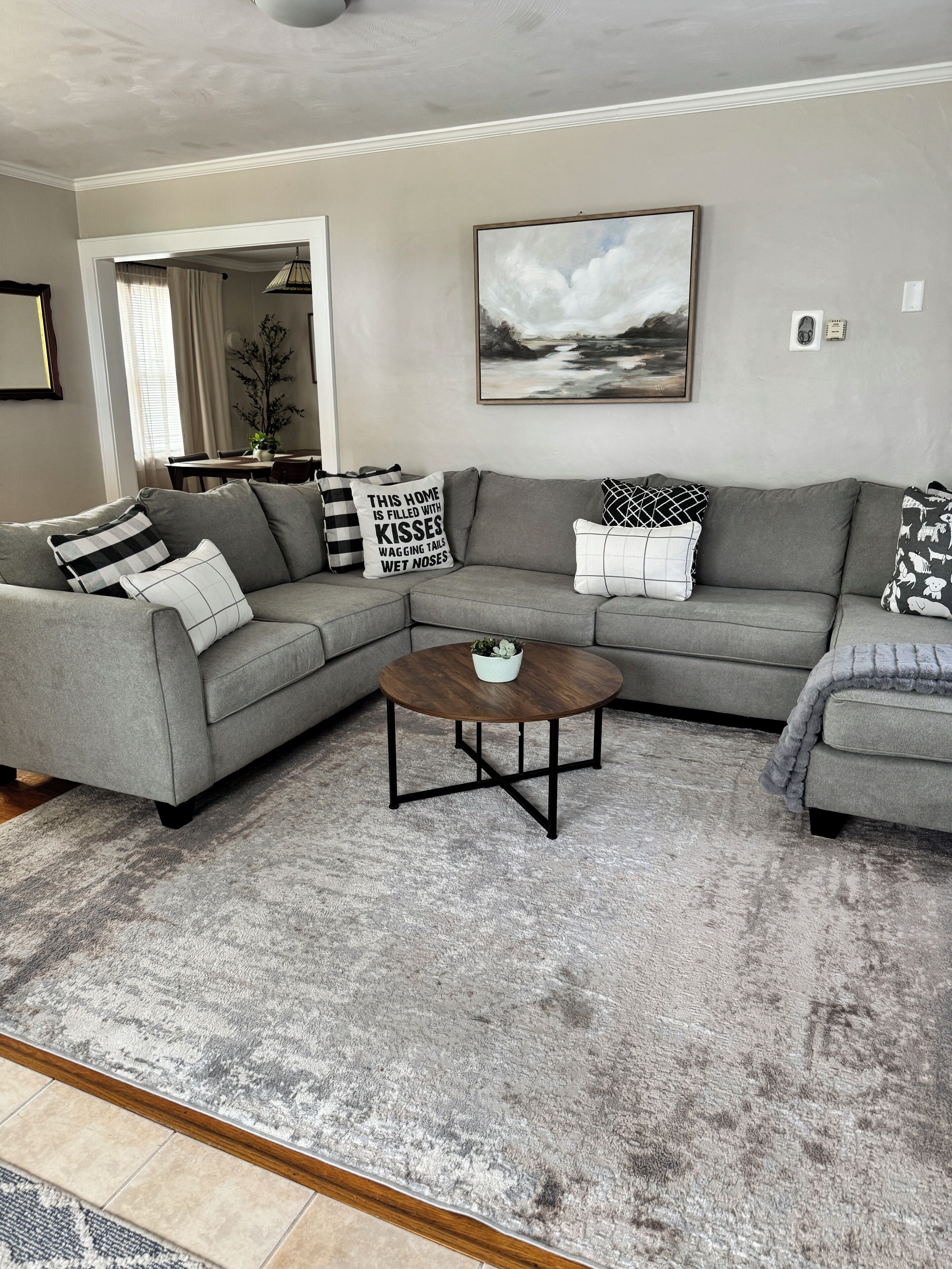 Ein Wohnzimmer mit einem grauen Ecksofa, einem runden Couchtisch und einem Bild an der Wand.