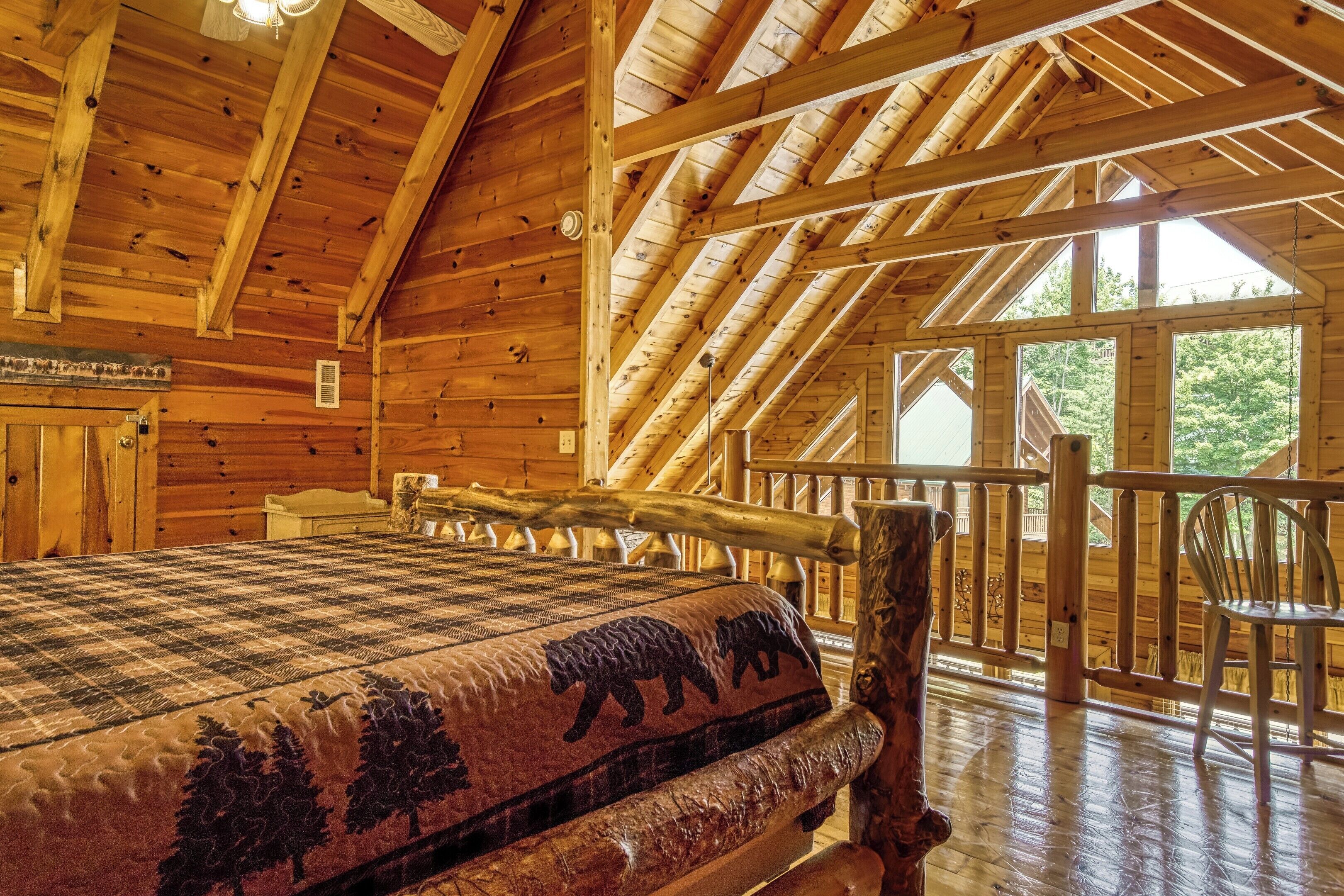A log cabin interior with a large bed, wooden beams, and a balcony with a railing.
