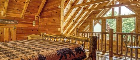 A log cabin interior with a large bed, wooden beams, and a balcony with a railing.