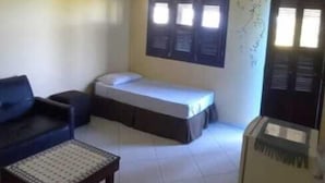 Een kleine, eenvoudige kamer met een bed, een slaapbank, een klein tafeltje en een koelkast.