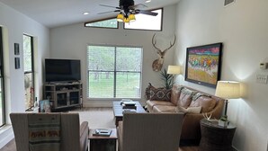 A living room with a television, leather sofa, and a ceiling fan. - Cool cottage on 30 acres between Blanco and Luckenbach (Blanco)