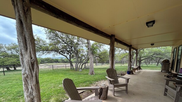 A covered outdoor seating area with wooden chairs and a metal watering can, overlooking a grassy landscape with trees. - Cool cottage on 30 acres between Blanco and Luckenbach (Blanco)
