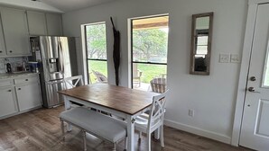 A modern kitchen with white cabinets, a stainless steel refrigerator, and a wooden dining table with white chairs. - Cool cottage on 30 acres between Blanco and Luckenbach (Blanco)