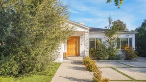 Une maison moderne avec une façade en pierre, une porte d’entrée en bois et une pelouse bien entretenue.