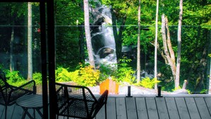 A deck with a view of a forest and a waterfall. - Loft Retreat on 24 acres with waterfall and hot tub (Highland Grove)