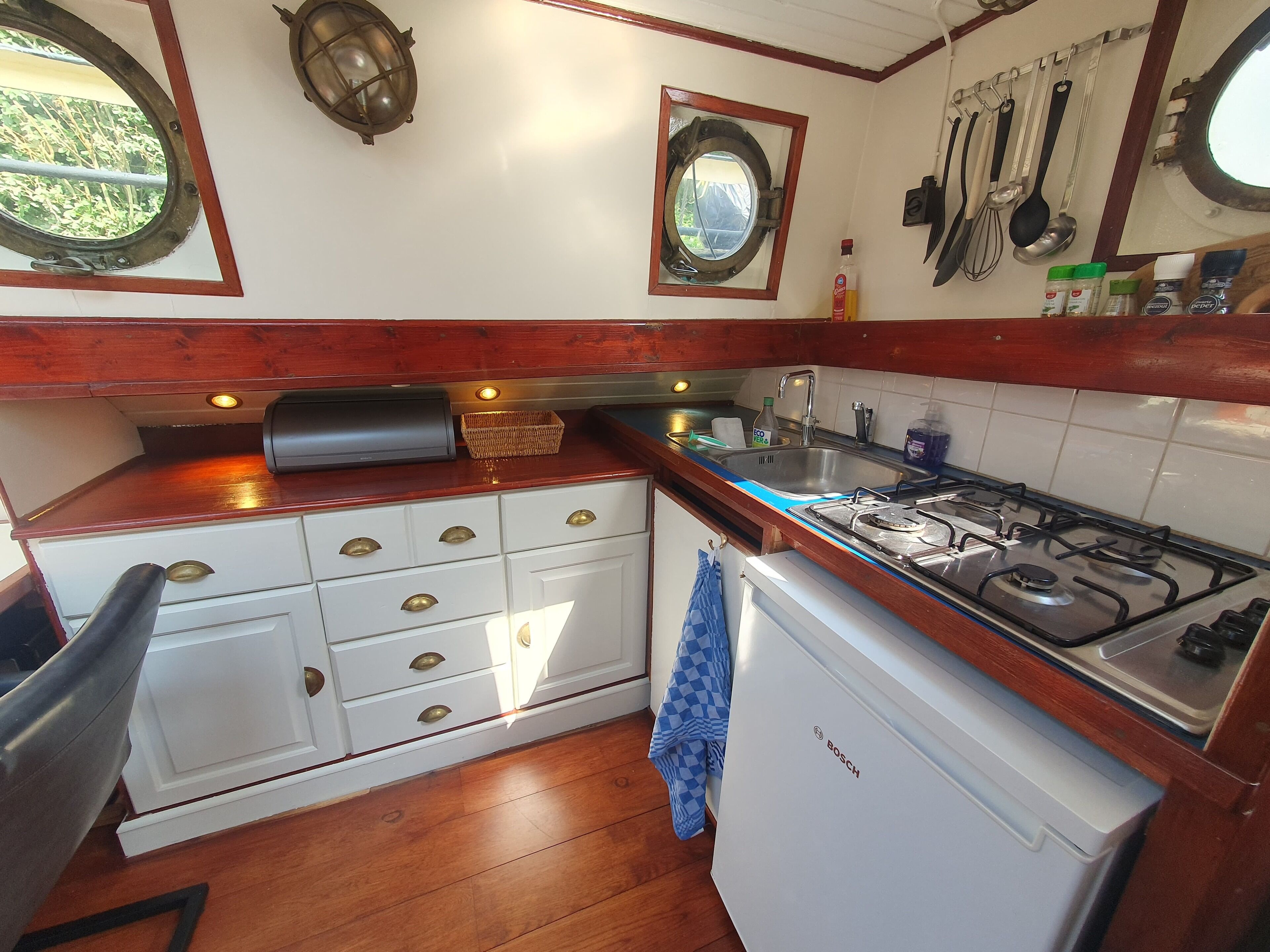 A kitchen with wooden cabinets, a Bosch refrigerator, a gas stove, and a window with a view of greenery.