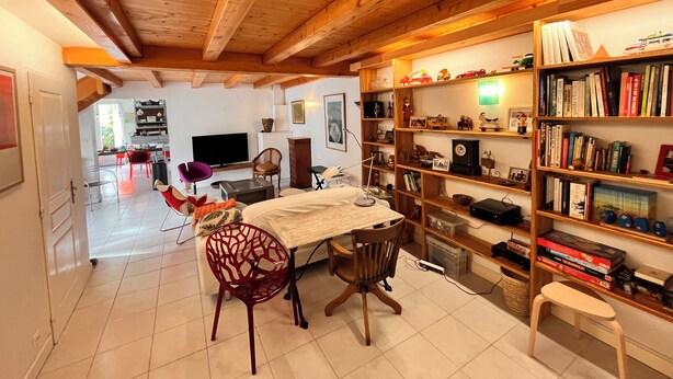 A cozy living room with a dining area, wooden ceiling beams, a bookshelf filled with books and decorative items, and a television. - Large family home 150 m from the beach, large well-equipped kitchen (Châtelaillon-Plage)