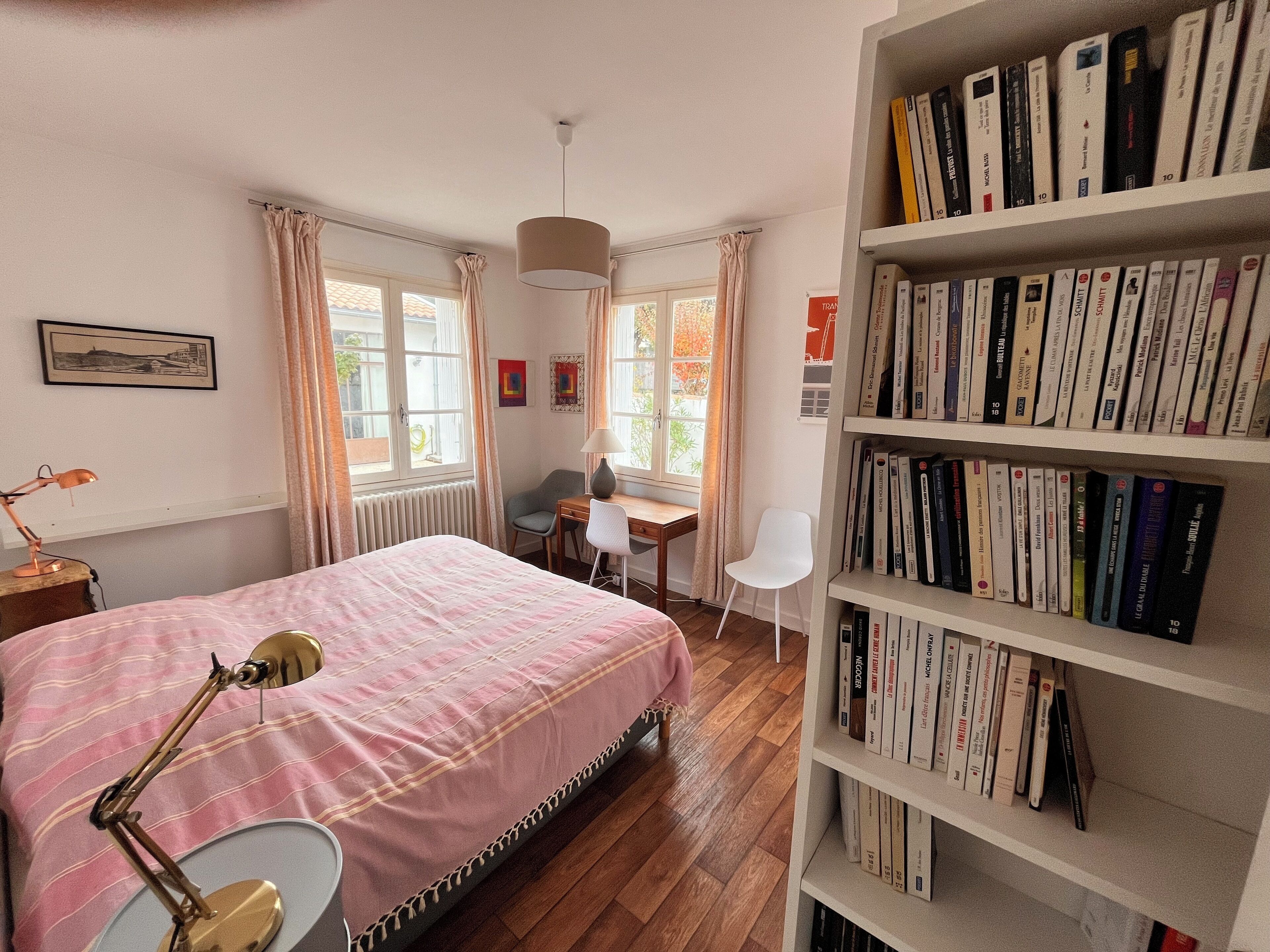 Een slaapkamer met een bed, een bureau, een stoel, een boekenkast en een raam met gordijnen.