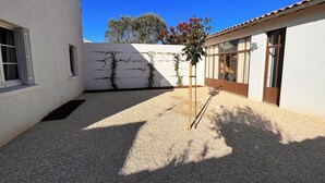 A courtyard with a gravel ground, white walls, and a small tree with red flowers. - Large family home 150 m from the beach, large well-equipped kitchen (Châtelaillon-Plage)