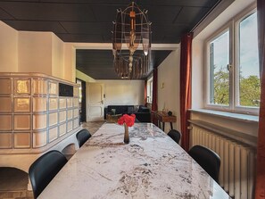 A dining area with a marble table, chairs, a vase with flowers, a chandelier, and a view through a window. - Villa Dora Petit Hôtel (Bad Reichenhall)