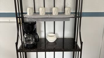 En svart metallhylla med tre våningar, där varje våning rymmer olika föremål, som till exempel burkar, muggar och en kaffebryggare.