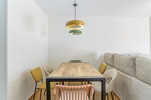 A dining area with a wooden table, four chairs, a sofa, and pendant lighting.