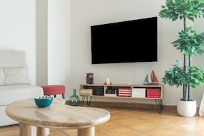 Una sala de estar con un sofá, una mesa de centro, un televisor montado en la pared, una estantería y una planta en maceta.
