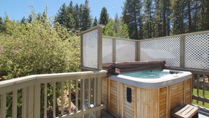 Een hottub op een houten terras, met een houten hek en bomen op de achtergrond.