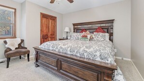 Een slaapkamer met een houten bed, een stoel, een plafondventilator en een raam met jaloezieën.