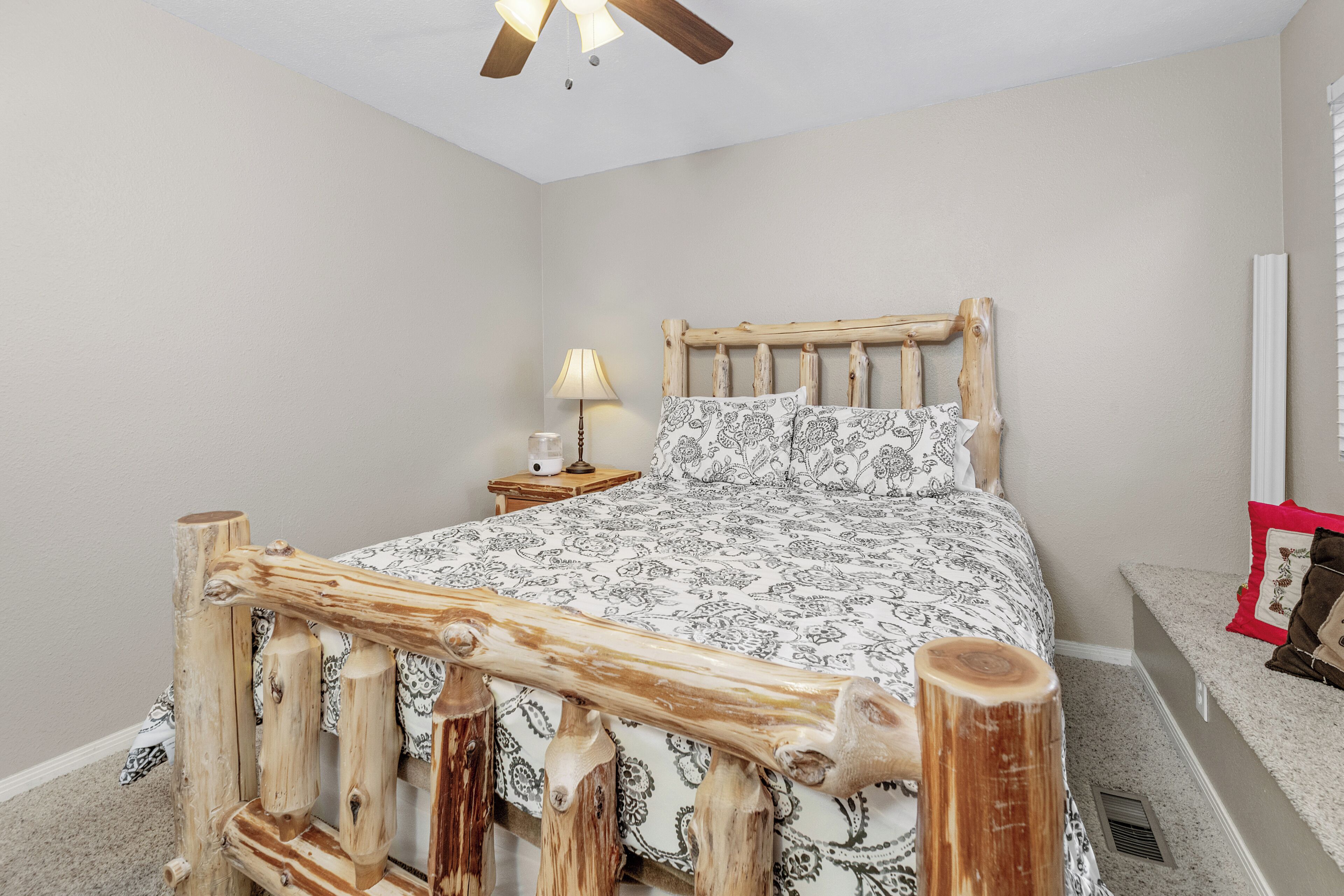 A bedroom with a wooden headboard, a bedside table with a lamp, and a patterned bedspread.