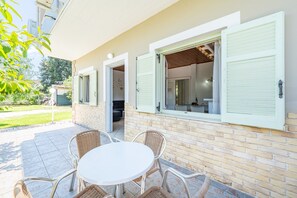 Um pátio com mesa redonda e cadeiras de vime, parede de tijolos e janela com persianas.