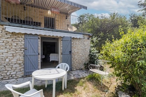 A stone house with a balcony, a round table with chairs, and a metal chair.