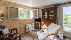 Une pièce aux murs de pierre, meublée en bois, avec une télévision et une vue sur la verdure environnante.