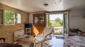 Une pièce comprenant un lit, un fauteuil à bascule, une armoire en bois, un téléviseur et une fenêtre donnant sur un paysage verdoyant.