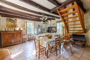 Une cuisine rustique avec des poutres en bois, une table à manger avec des chaises, un escalier et un téléviseur.