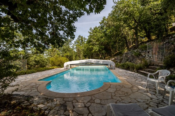 Une piscine aux bords recouverts de pierres, entourée de verdure et agrémentée d’escaliers en pierre.