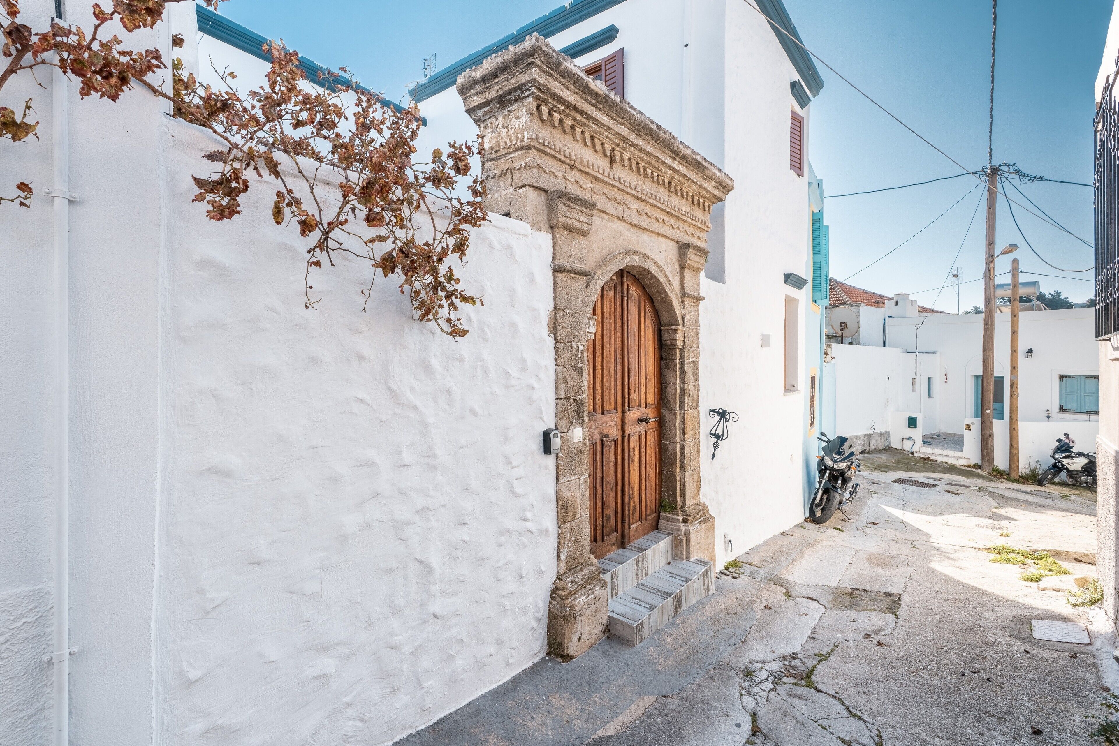 A narrow street with a white building featuring a wooden door and steps leading to the entrance.