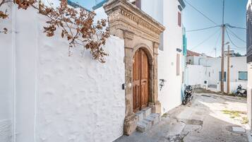 A narrow street with a white building featuring a wooden door and steps leading to the entrance.