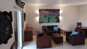 Un soggiorno con un grande quadro raffigurante una scena tropicale, un divano, due poltrone e un tavolino.