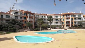 Ein Hotel mit mehreren Etagen, Außenpools und einer angelegten Grünfläche mit Palmen.