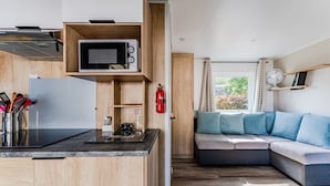 Une cuisine compacte équipée d’un four à micro-ondes, d’une cuisinière et d’une machine à café, d’un meuble en bois et d’un coin salon confortable avec des coussins.
