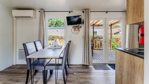 Une cuisine moderne dotée d’un téléviseur encastré, d’un coin repas avec une table et des chaises, et d’une porte-fenêtre coulissante donnant sur une terrasse extérieure.