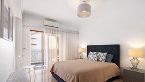 Ein Schlafzimmer mit einem Bett, Nachttischen, einem Sessel und einem Fenster mit Vorhängen.