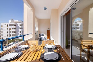 Un balcón con una mesa de madera dispuesta para comer, una silla y vistas a un edificio.
