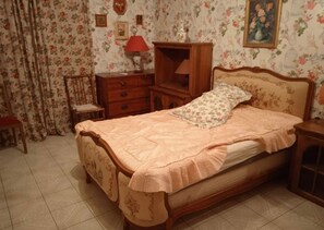 Quarto com cama, mesa de cabeceira, penteadeira, uma cadeira e papel de parede floral.