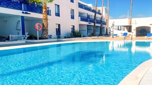 A clear swimming pool with a blue sky above, surrounded by a building with balconies and a white fence. - Apartment Bellissima With Pool and Wi-fi, 200m From the sea in Puerto del Carmen (Tías)