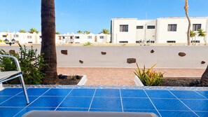 A pool area with blue tiles, a palm tree, and a view of white buildings in the background. - Apartment Bellissima With Pool and Wi-fi, 200m From the sea in Puerto del Carmen (Tías)