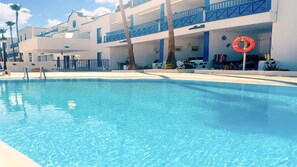 A clear blue pool with a lifebuoy, palm trees, and a building with balconies. - Apartment Bellissima With Pool and Wi-fi, 200m From the sea in Puerto del Carmen (Tías)