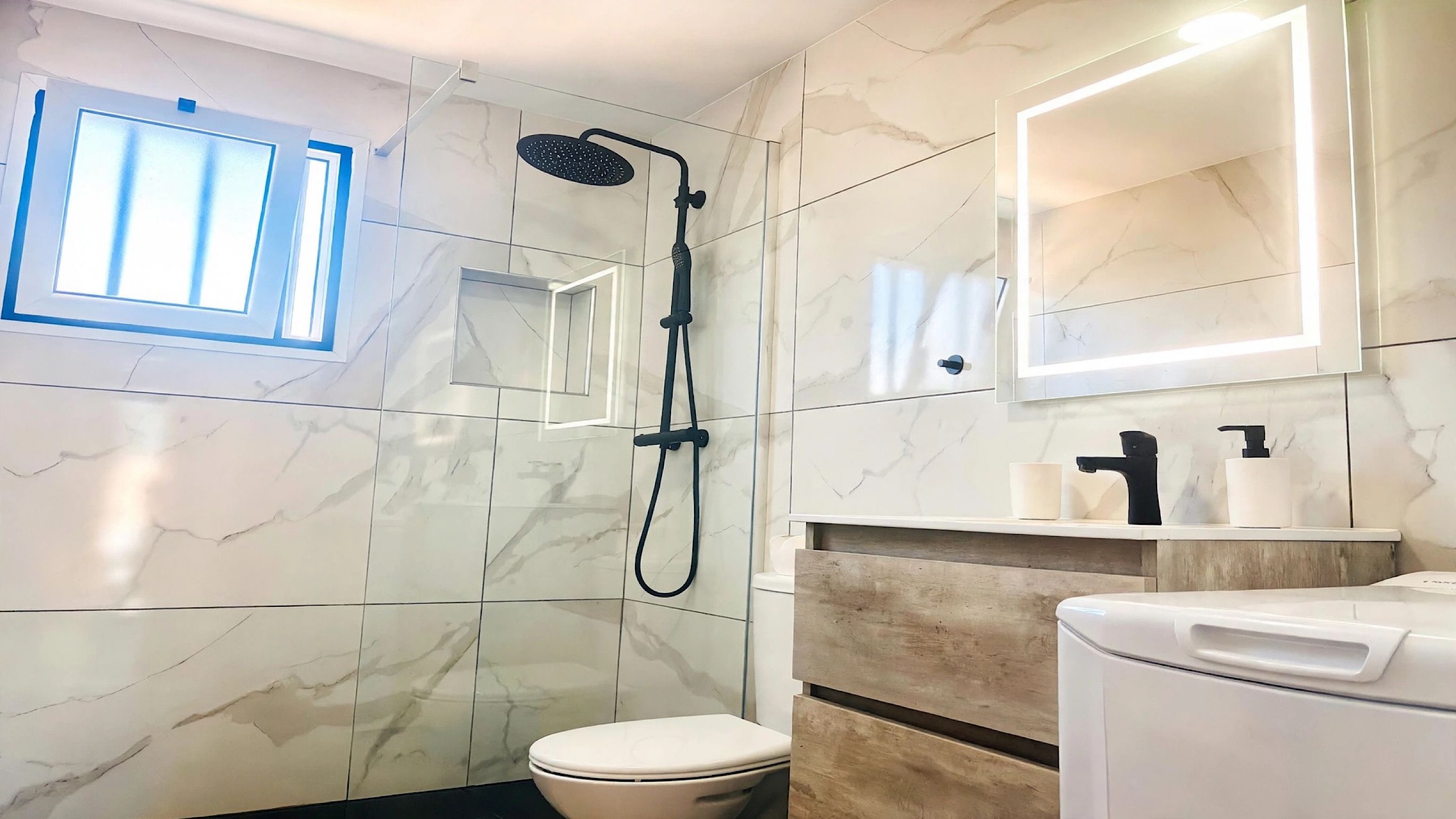 Un baño con ducha, inodoro y espejo con iluminación integrada.