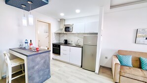 A modern kitchen with white cabinets, a stainless steel refrigerator, and a microwave. There's a dining area with a table and chairs, and a beige sofa with patterned cushions. - Apartment Bellissima With Pool and Wi-fi, 200m From the sea in Puerto del Carmen (Tías)