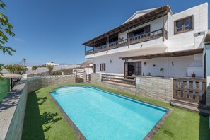 Una casa a due piani con piscina, un balcone e un muro in pietra.