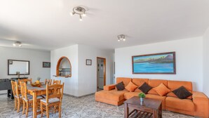 Amplia sala de estar con una mesa de comedor, sofá naranja y un cuadro en la pared.