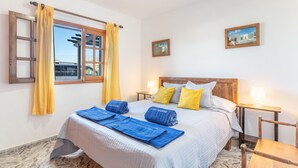 Una habitación de hotel con una cama, dos mesitas de noche, un cabecero de madera, un ventanal con cortinas y un cuadro colgado en la pared.
