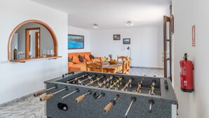 Una habitación con una mesa de fútbol de mesa, un espejo, un sofá, una mesa de comedor con sillas y un extintor.
