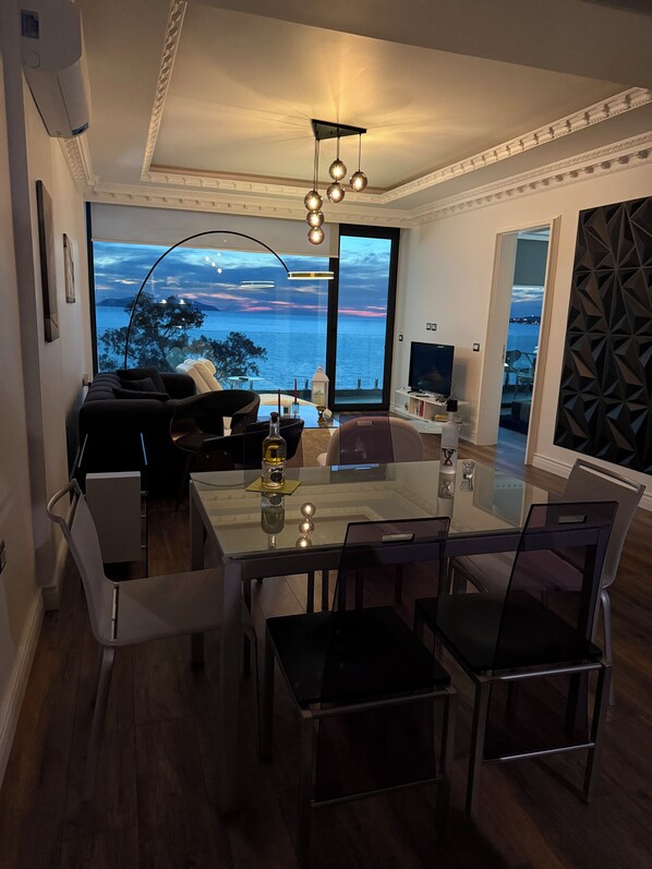 A modern dining area with a glass table, chairs, and a view of the sea.