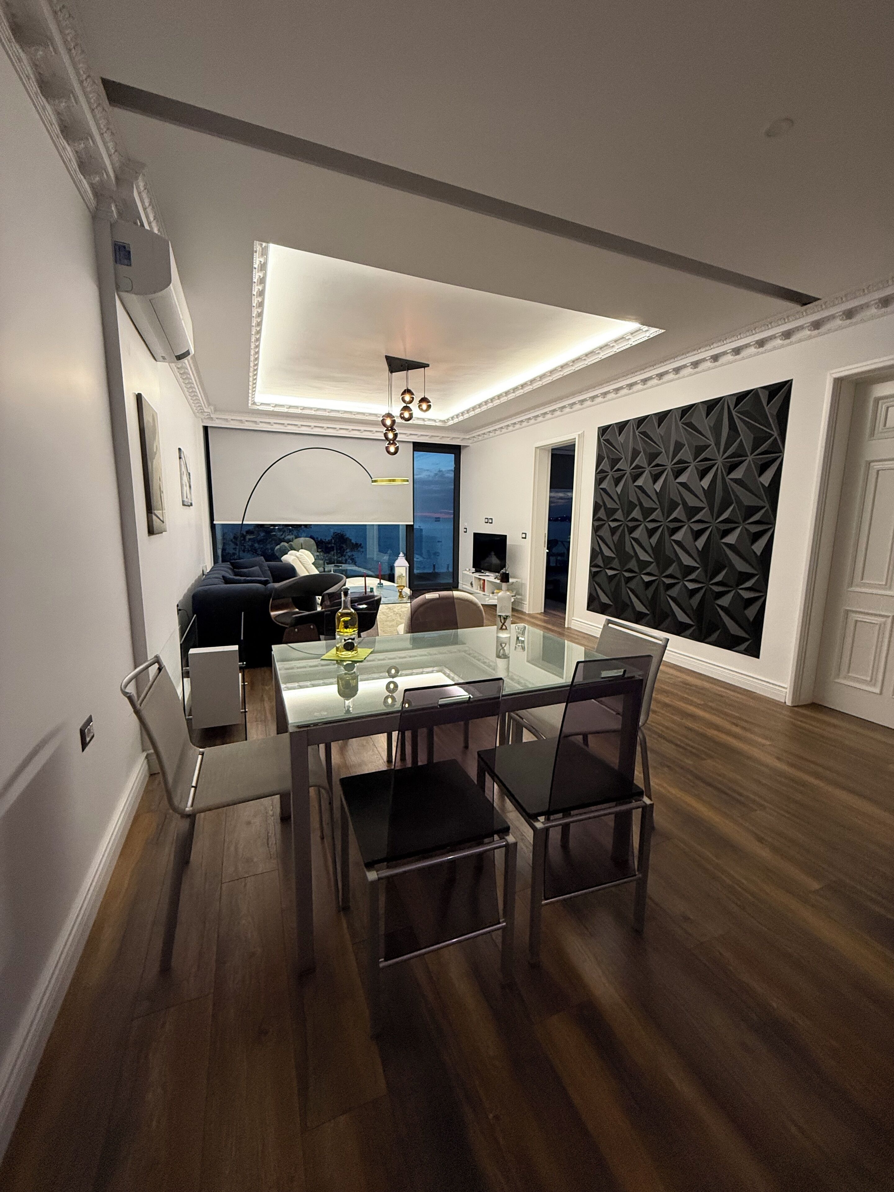 Ein modernes Wohnzimmer mit einem Glastisch, dunklem Holzboden und einer geometrischen Wandverkleidung.