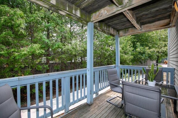 A covered outdoor deck with blue railings, two chairs, and a potted plant.